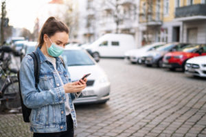 Woman wearing a medical mask and using a phone outdoors
